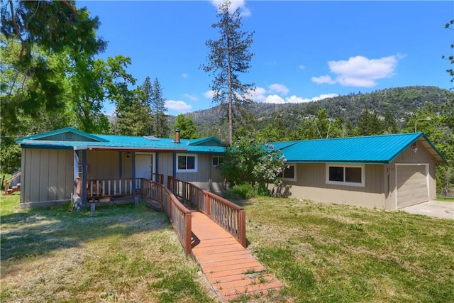 rear view of house with metal roof, a detached garage, a mountain view, and a lawn