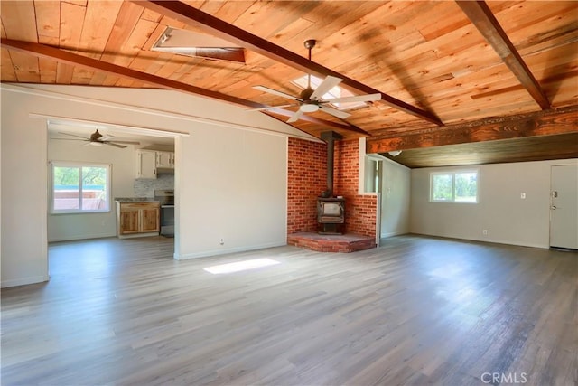 unfurnished living room with a wealth of natural light, lofted ceiling with beams, a wood stove, and wooden ceiling