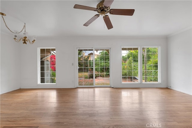 spare room with crown molding, baseboards, wood finished floors, and ceiling fan with notable chandelier