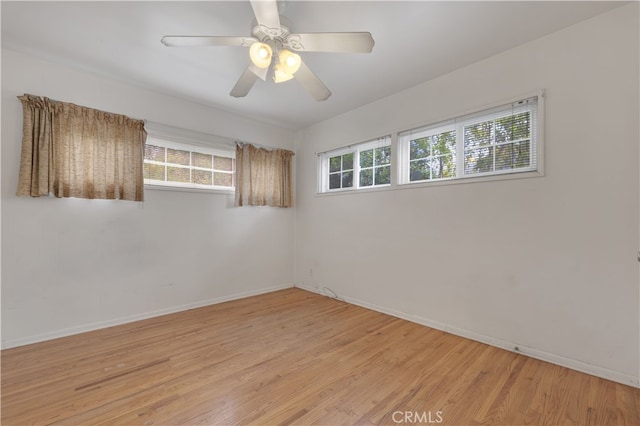 empty room featuring a wealth of natural light, baseboards, a ceiling fan, and light wood-style floors
