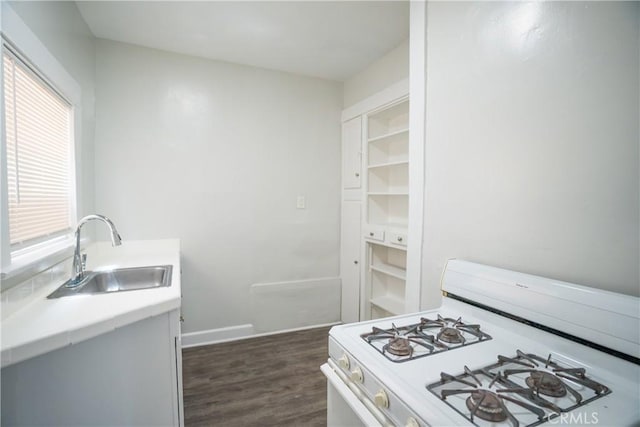 kitchen with baseboards, white gas range, a sink, dark wood-type flooring, and light countertops