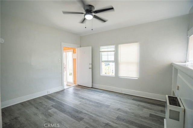 empty room featuring a ceiling fan, baseboards, heating unit, and wood finished floors