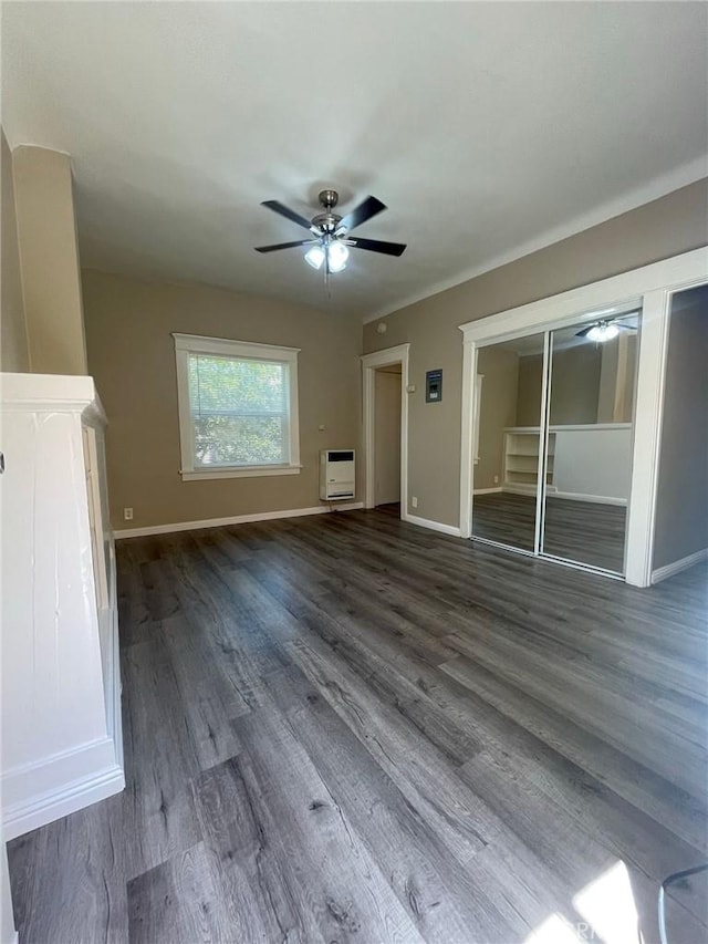 unfurnished living room featuring heating unit, baseboards, dark wood-style flooring, and a ceiling fan