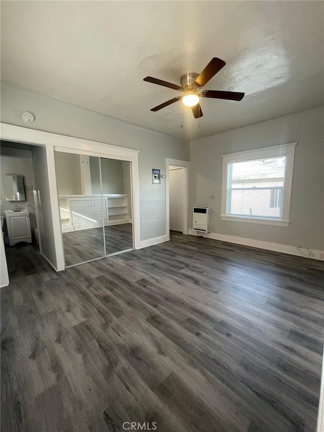 unfurnished living room with heating unit, dark wood-type flooring, baseboards, and ceiling fan