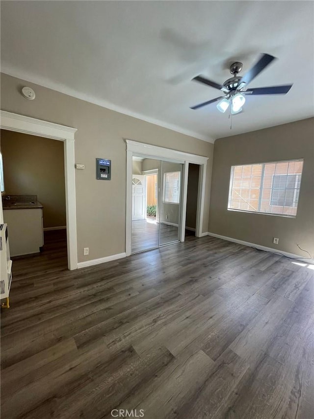 interior space with baseboards, a ceiling fan, and dark wood-type flooring