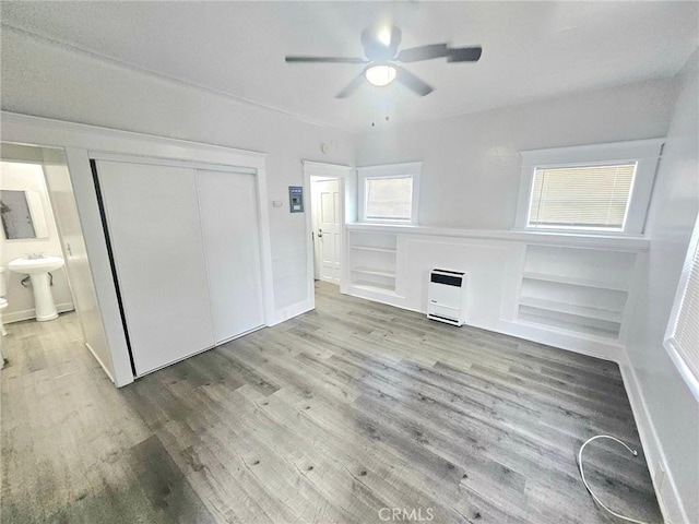 unfurnished living room with heating unit, wood finished floors, a ceiling fan, and a sink