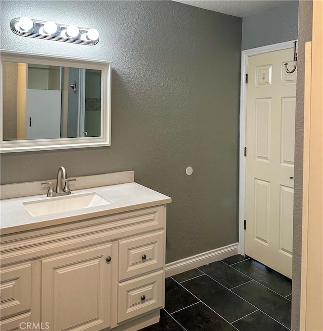 bathroom featuring tile patterned floors, vanity, a textured wall, and baseboards