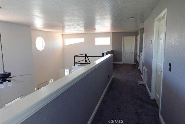 corridor with an upstairs landing, dark colored carpet, a textured ceiling, and baseboards
