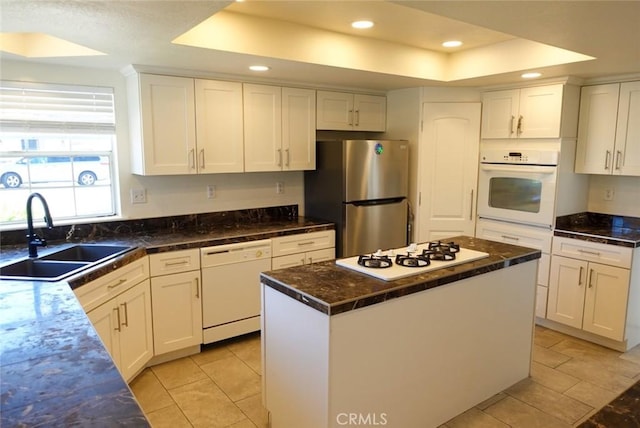 kitchen with white appliances, a tray ceiling, a sink, white cabinets, and recessed lighting