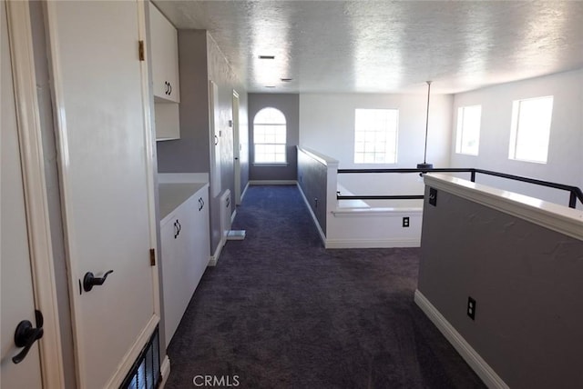 hall with dark carpet, baseboards, and a textured ceiling