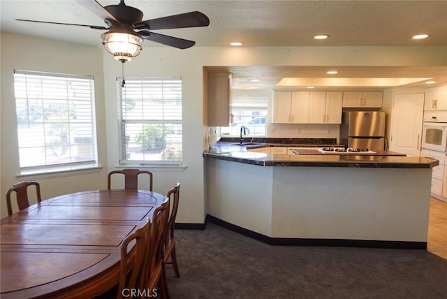 kitchen with freestanding refrigerator, white oven, dark countertops, a peninsula, and a sink