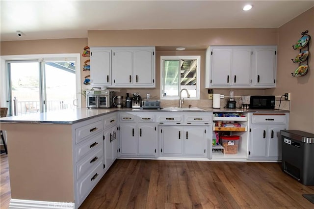 kitchen featuring dark wood-style flooring, a peninsula, black microwave, and white cabinets