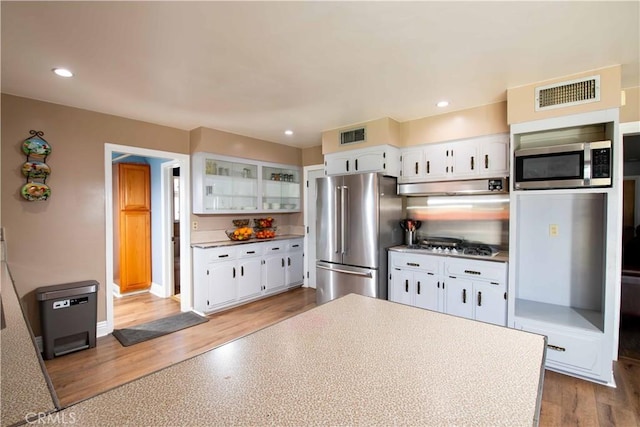 kitchen with glass insert cabinets, white cabinetry, visible vents, under cabinet range hood, and appliances with stainless steel finishes