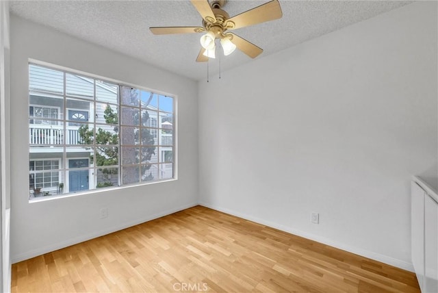 empty room featuring baseboards, light wood-style floors, ceiling fan, and a textured ceiling