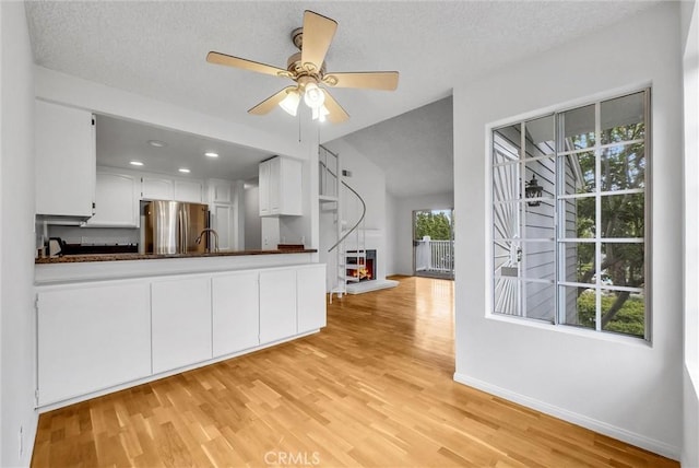 unfurnished living room featuring a warm lit fireplace, baseboards, light wood finished floors, ceiling fan, and a sink