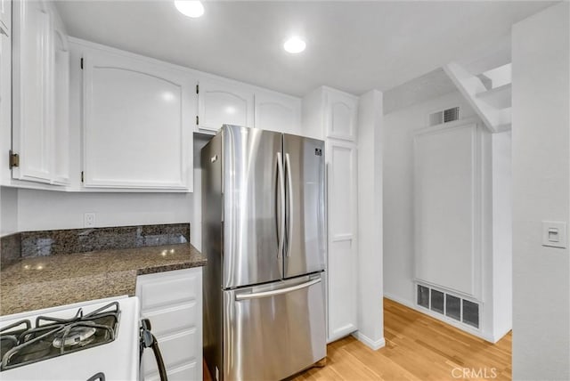 kitchen with white gas range oven, freestanding refrigerator, white cabinetry, and visible vents