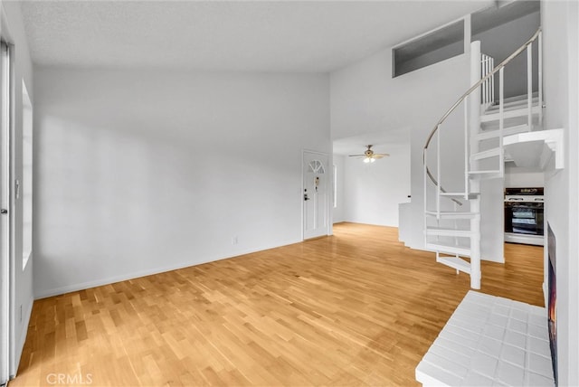 interior space with stairs, high vaulted ceiling, ceiling fan, baseboards, and light wood-style floors