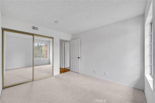 unfurnished bedroom featuring a textured ceiling, carpet floors, a closet, and visible vents
