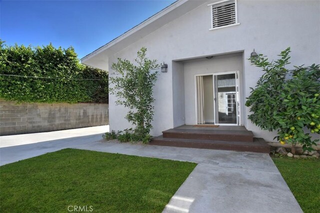 view of exterior entry with a yard and stucco siding
