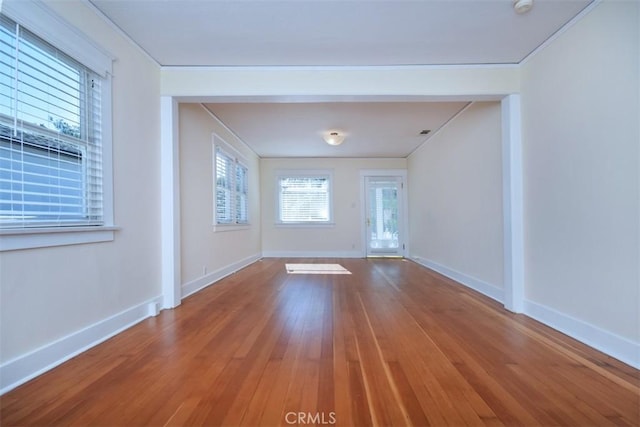 empty room with crown molding, baseboards, and wood-type flooring