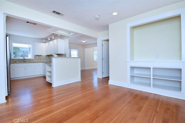 kitchen featuring rail lighting, built in shelves, plenty of natural light, white cabinets, and light wood-style floors