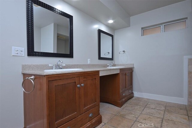 full bath featuring baseboards, stone tile floors, a sink, and double vanity