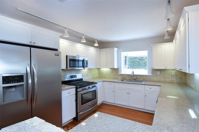 kitchen with a sink, stainless steel appliances, track lighting, white cabinetry, and decorative backsplash