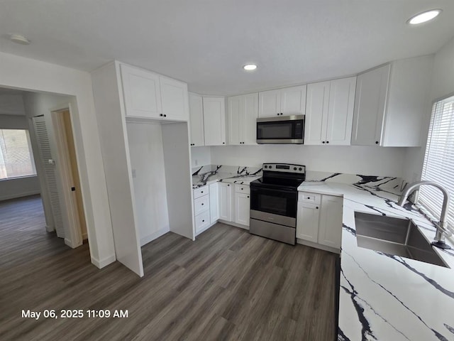kitchen with a sink, white cabinets, dark wood-type flooring, light stone countertops, and appliances with stainless steel finishes