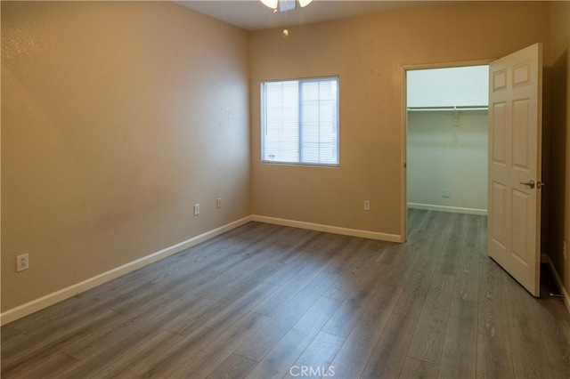 unfurnished bedroom with a spacious closet, baseboards, dark wood-style floors, and a closet