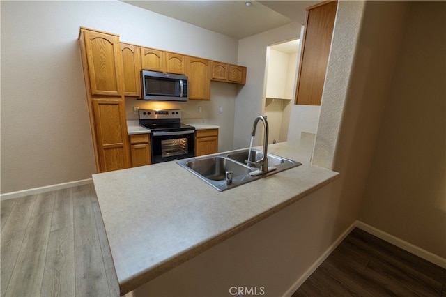 kitchen with a peninsula, wood finished floors, a sink, black range with electric stovetop, and stainless steel microwave