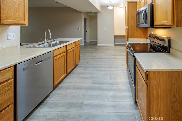 kitchen with brown cabinets, a sink, stainless steel appliances, light wood-type flooring, and light countertops
