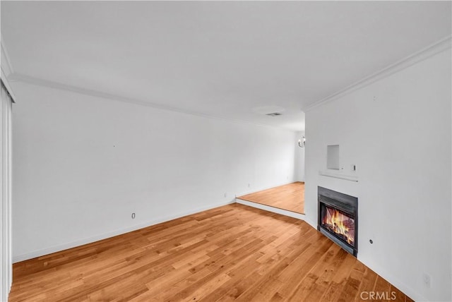 unfurnished living room with light wood-type flooring, baseboards, a glass covered fireplace, and crown molding