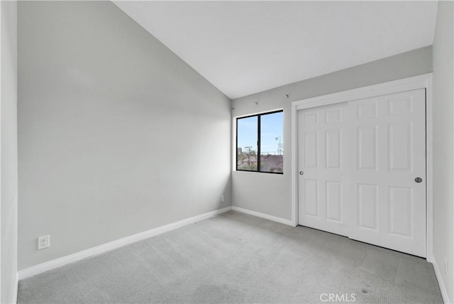 unfurnished bedroom featuring carpet flooring, a closet, vaulted ceiling, and baseboards