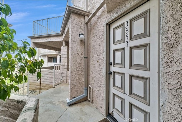 view of exterior entry featuring a balcony and stucco siding