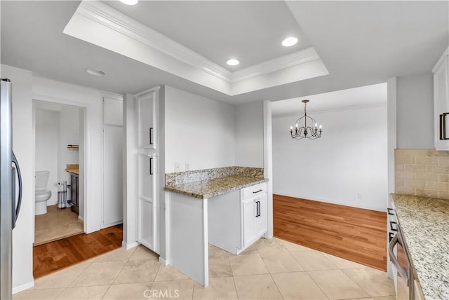 kitchen with a tray ceiling, crown molding, a chandelier, and light tile patterned flooring