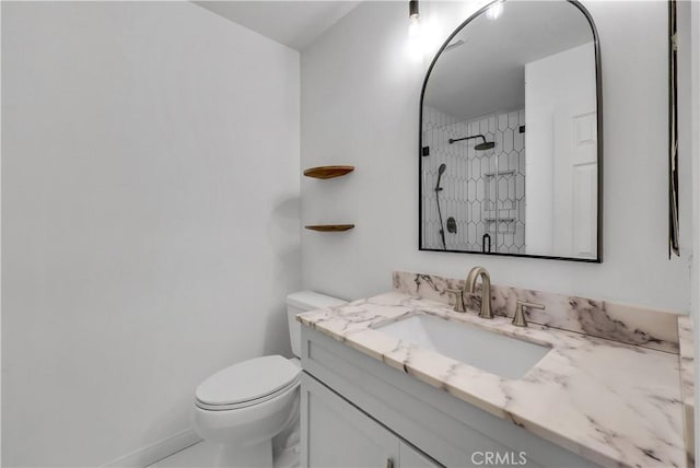 bathroom featuring toilet, tiled shower, and vanity