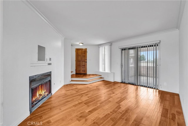 unfurnished living room featuring light wood finished floors, crown molding, a warm lit fireplace, and baseboards