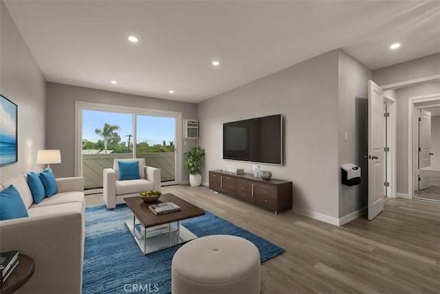 living area featuring a wall mounted air conditioner, a baseboard heating unit, wood finished floors, recessed lighting, and baseboards