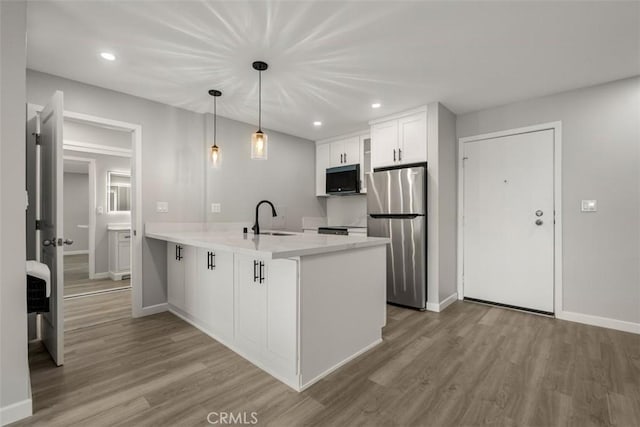 kitchen featuring freestanding refrigerator, a peninsula, a sink, and wood finished floors
