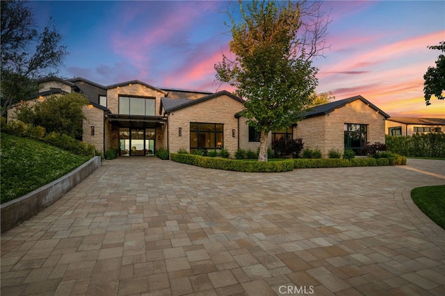 view of front of house with curved driveway, solar panels, and stone siding