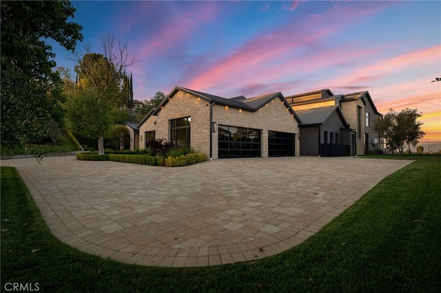 view of side of property featuring stone siding, decorative driveway, a garage, and a yard