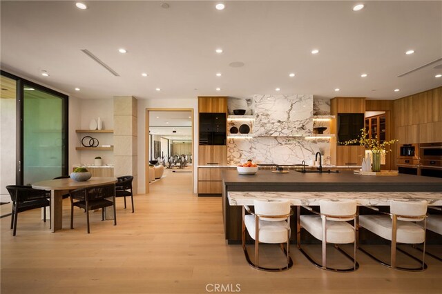 25079 Jim Bridger Rd, Hidden Hills, CA 91302 - kitchen with light wood finished floors, brown cabinets, a sink, modern cabinets, and a large island with sink