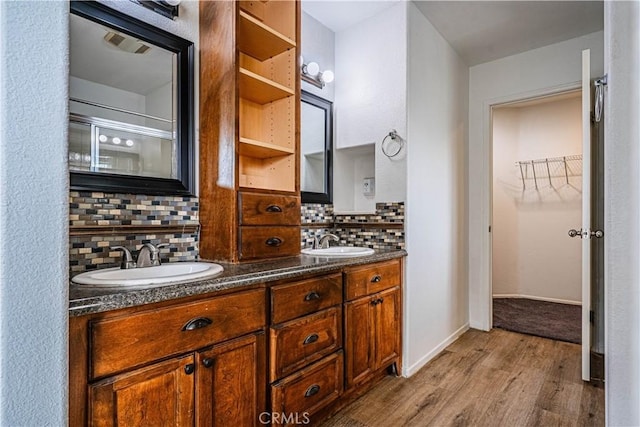 bathroom with a sink, a spacious closet, backsplash, and wood finished floors