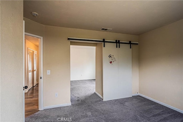 empty room featuring carpet, visible vents, a barn door, and baseboards