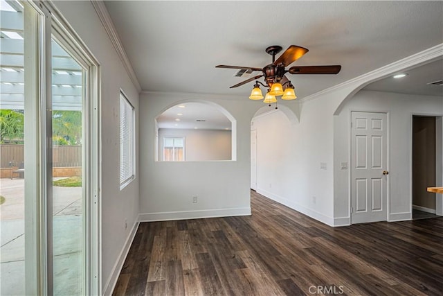 spare room featuring baseboards, dark wood finished floors, ceiling fan, crown molding, and arched walkways