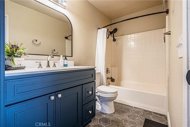bathroom featuring toilet, tile patterned floors, a textured wall, shower / bathtub combination with curtain, and vanity