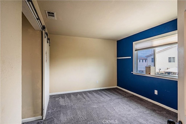carpeted empty room with baseboards, a barn door, and visible vents