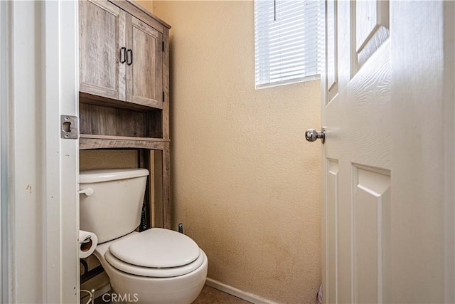 bathroom featuring toilet, baseboards, and a textured wall