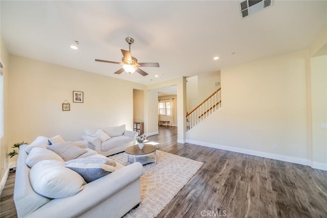 living area with wood finished floors, a ceiling fan, visible vents, baseboards, and stairway