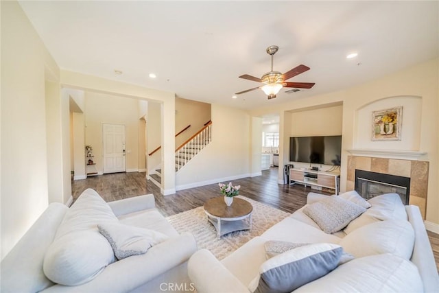 living area with wood finished floors, a fireplace, ceiling fan, and stairs